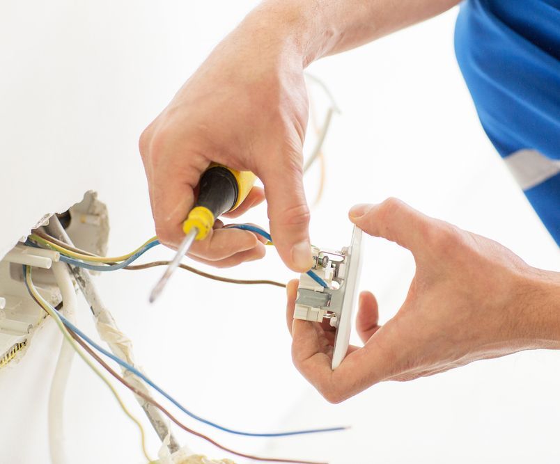 A person is fixing an electrical outlet with a screwdriver