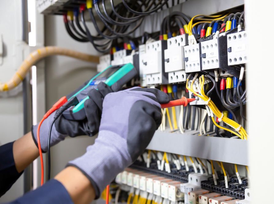 An electrician is working on an electrical panel with a multimeter
