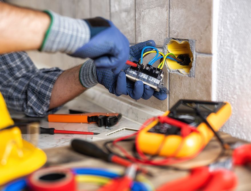 An electrician is working on an electrical outlet on a wall