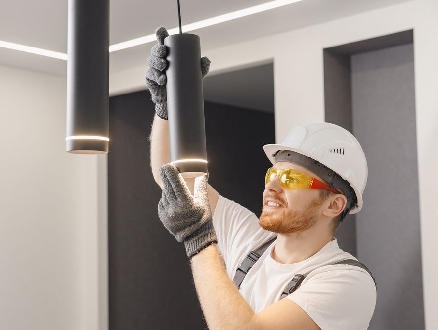 A man wearing a hard hat and safety glasses is installing a light fixture