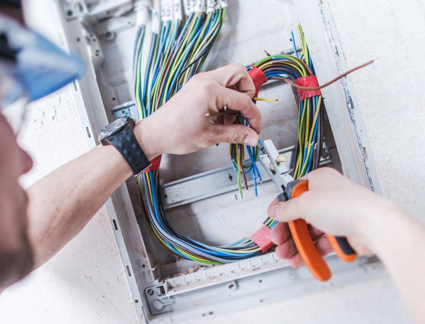 A man is working on an electrical box with a pair of pliers