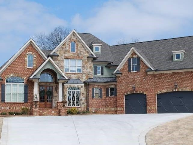 Large brick and stone house with a driveway and dark garage doors under a blue sky.