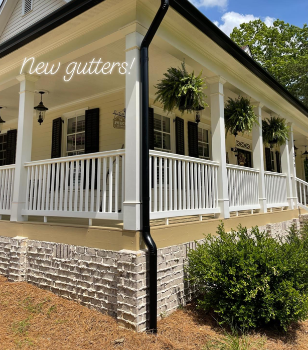 White porch with new black gutters and hanging plants.