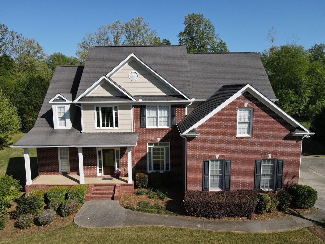Two-story house with brick and siding, front porch, dark roof, surrounded by trees.