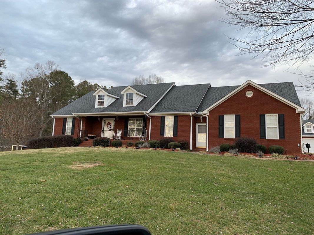 Brick ranch house with black shutters, dormers, and a green lawn.