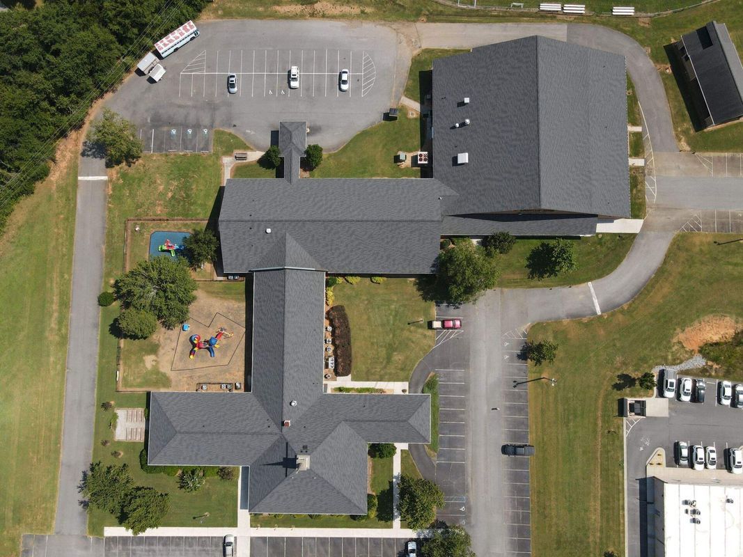 Aerial view of a gray-roofed building complex with parking, green space, and a playground.