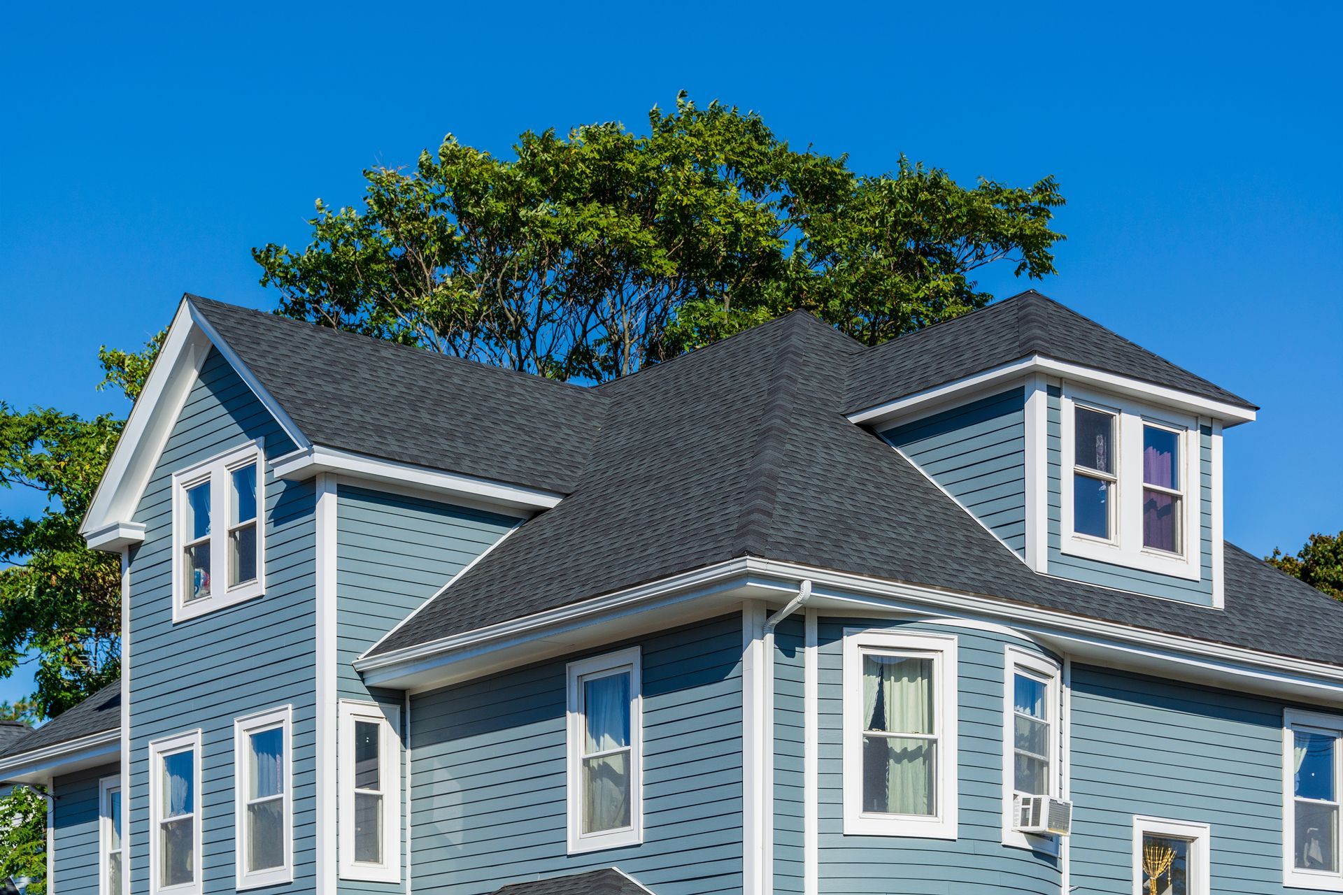 Blue house with dark gray roof, white trim, and a clear blue sky.