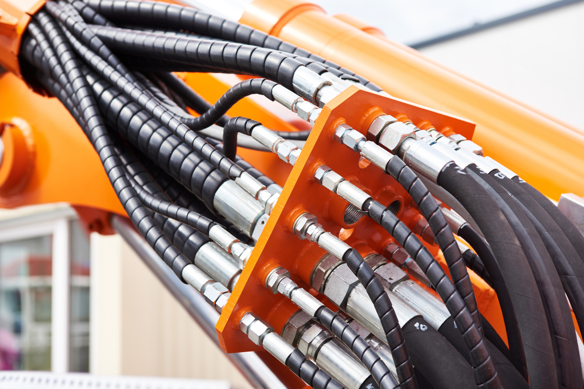 Coiled black hydraulic hoses with silver fittings on an orange industrial machine