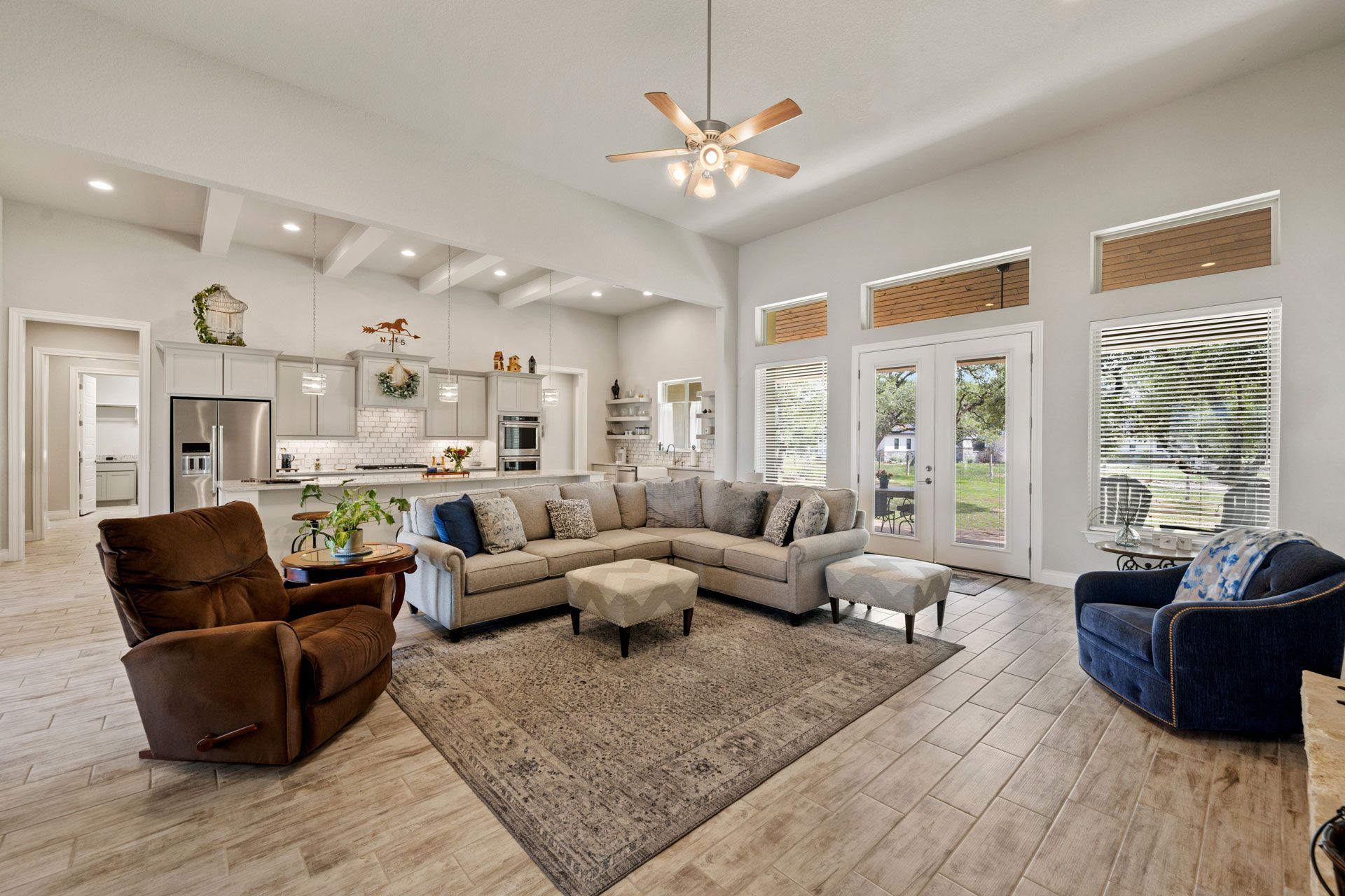 Spacious living room with sectional sofa, recliner, and kitchen in background. Bright with large windows.