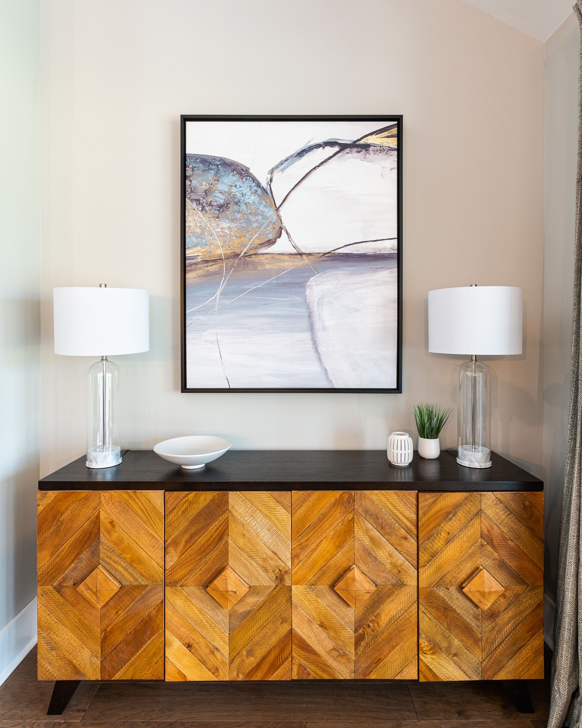 Wooden cabinet with art and lamps against a tan wall.