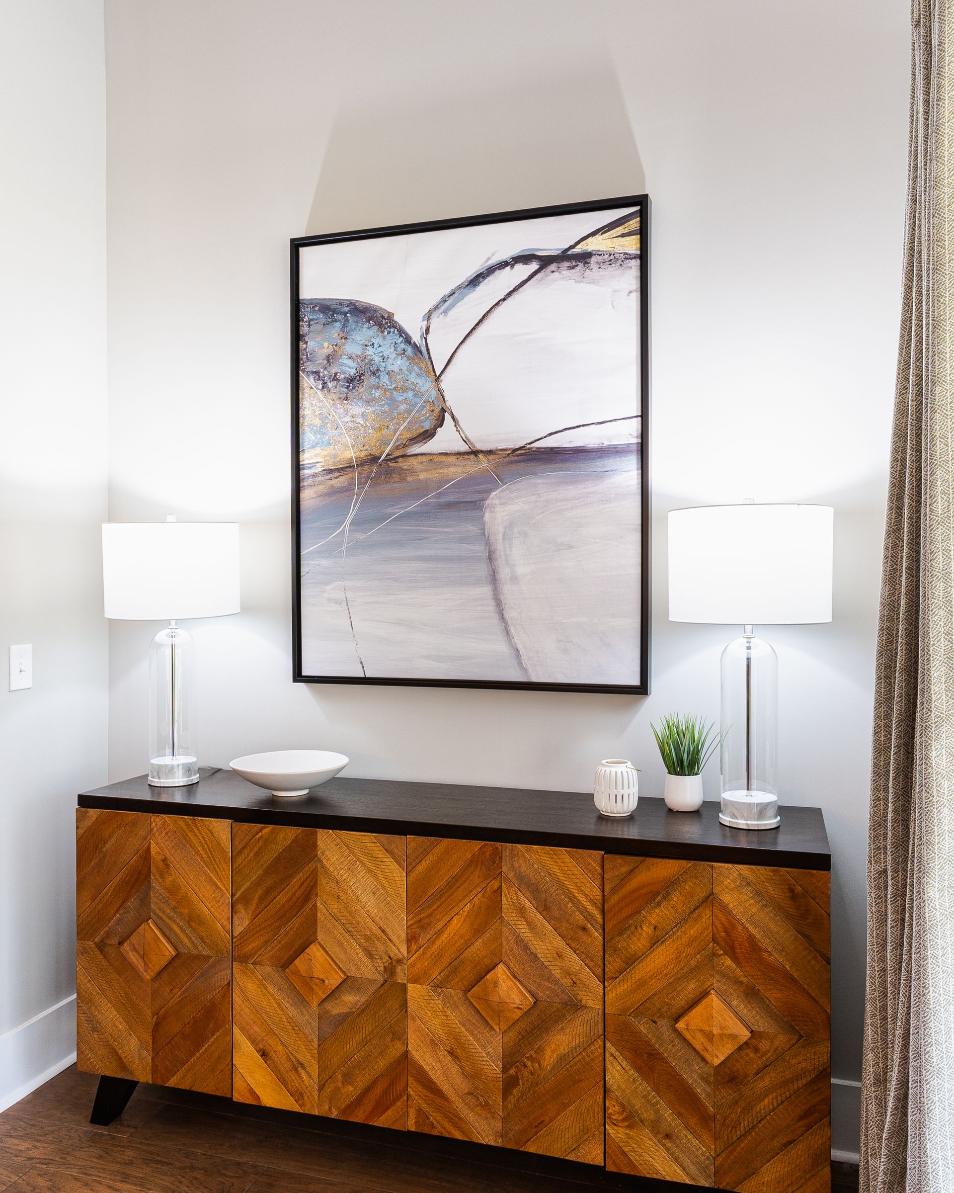 Wooden cabinet with artwork and lamps against a gray wall.