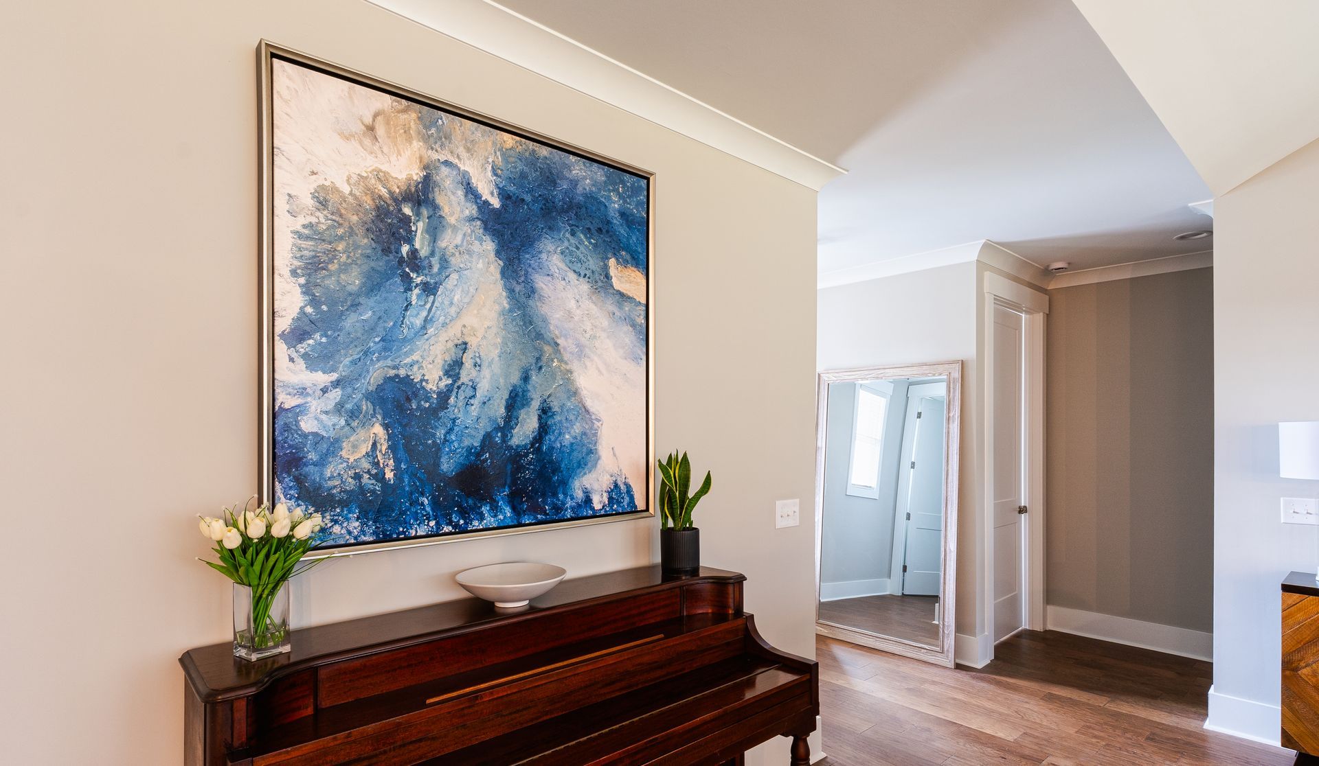 Entryway with piano, large blue abstract painting, flowers, and hallway with open doors.