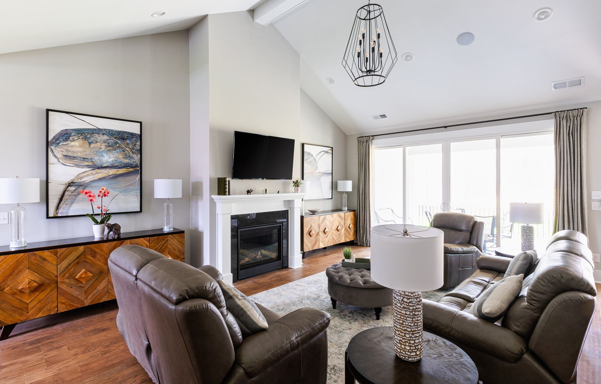 Living room with fireplace, brown leather furniture, artwork, and large windows.