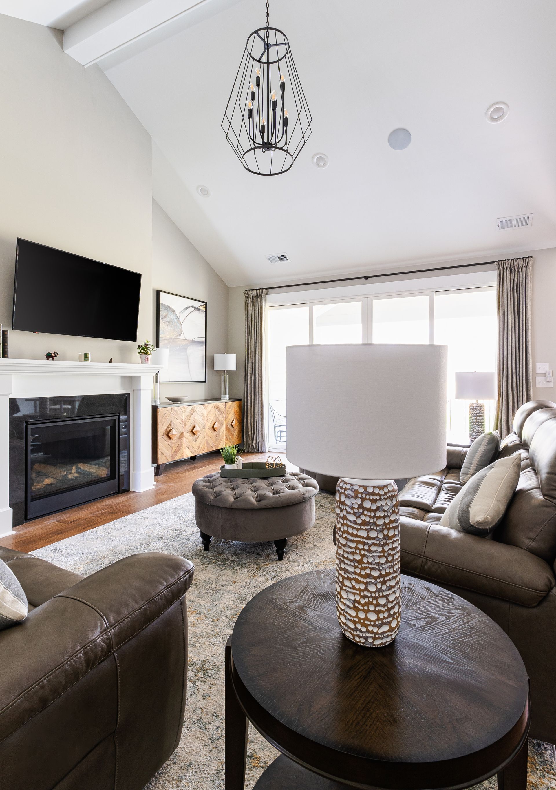 Living room with fireplace, leather furniture, rug, pendant light, and accent table with lamp.