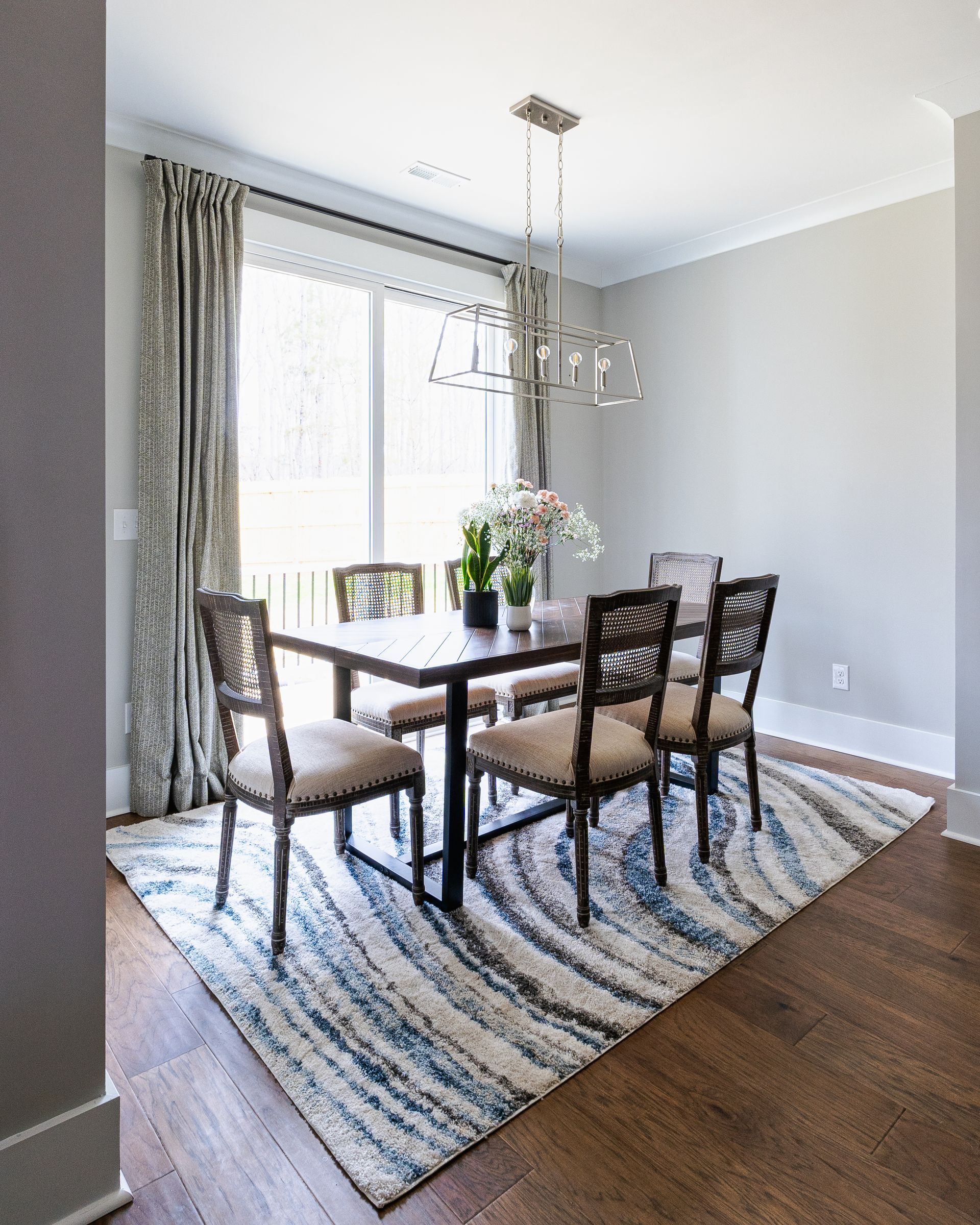 Dining room with a dark wood table, six chairs, patterned rug, and floral centerpiece.