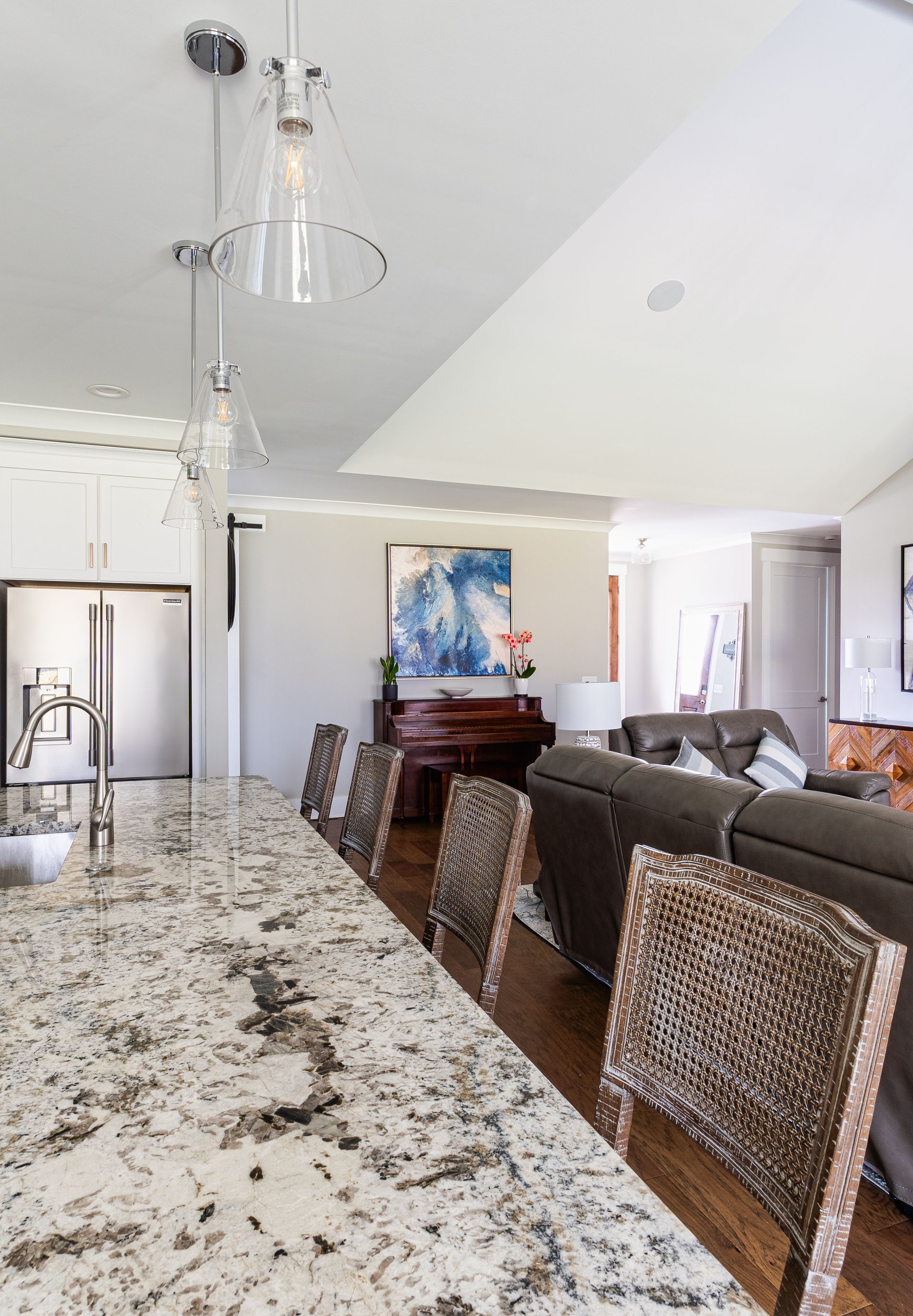 Kitchen island with granite countertop, pendant lights, and woven bar stools; living area visible beyond.