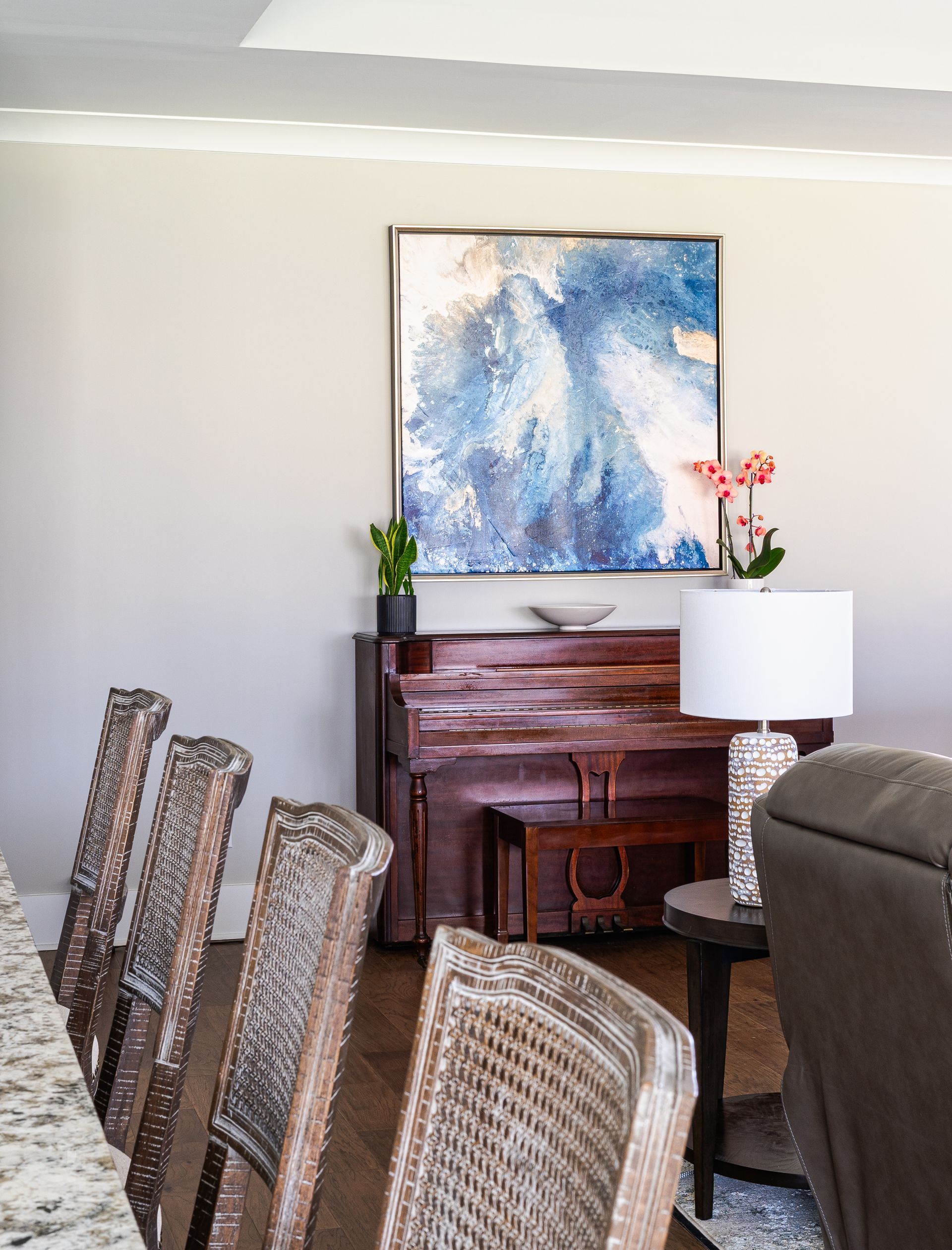 Dining room with a piano and painting, chairs, lamp, flowers, in neutral colors.