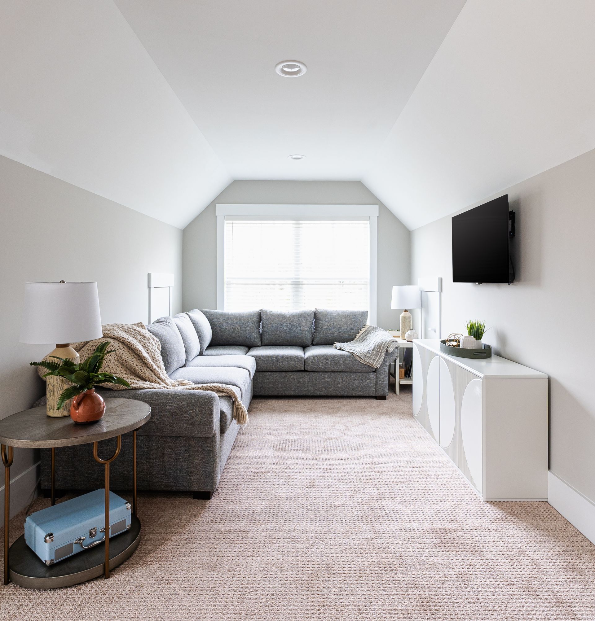 Cozy attic living room with a gray sectional sofa, a mounted TV, and a pink rug.
