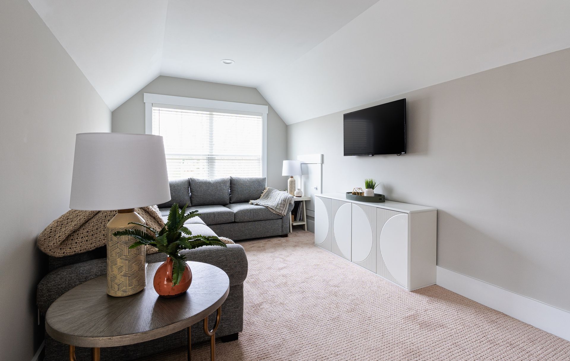 Cozy attic living room with gray sofa, patterned rug, TV, and decorative console.