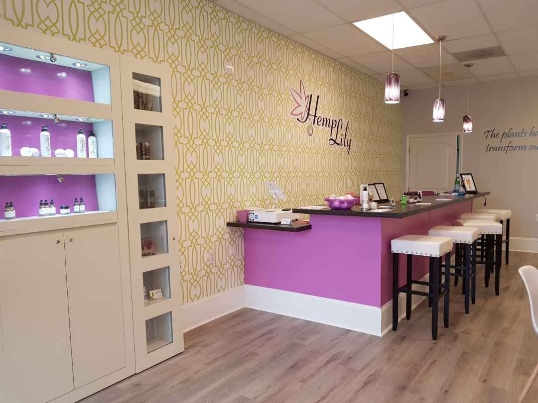 A pink and yellow salon interior with a display cabinet, a counter with stools, and floral wallpaper.