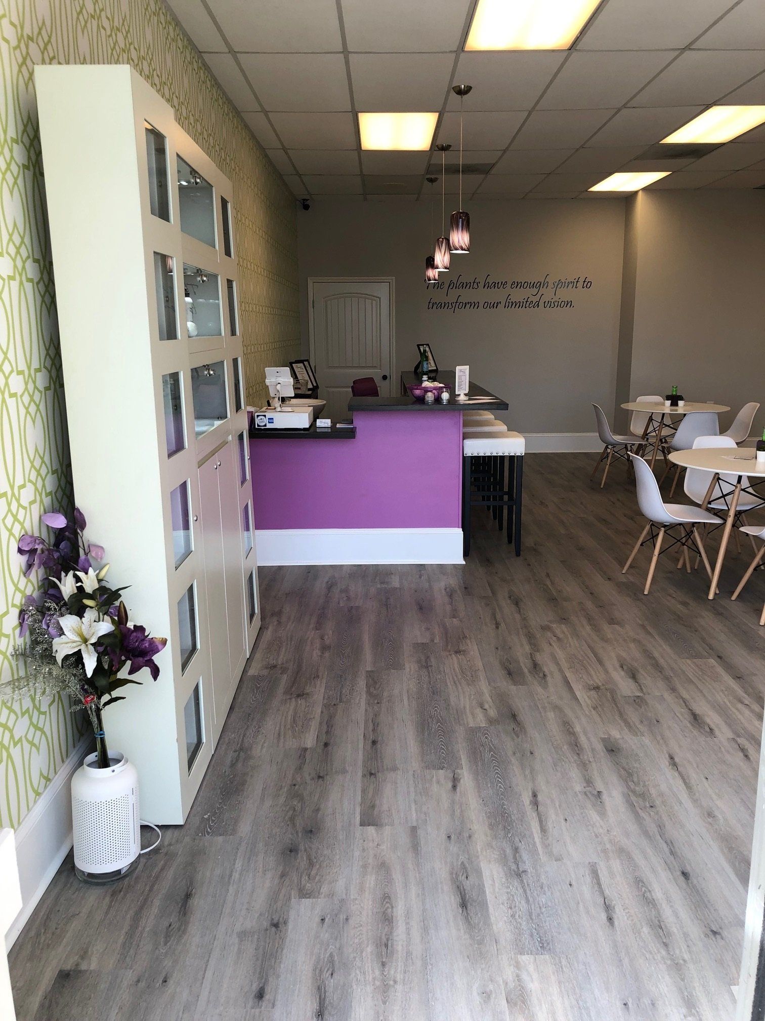 Interior view of a cafe with a purple counter, white chairs, and gray wood-look flooring.