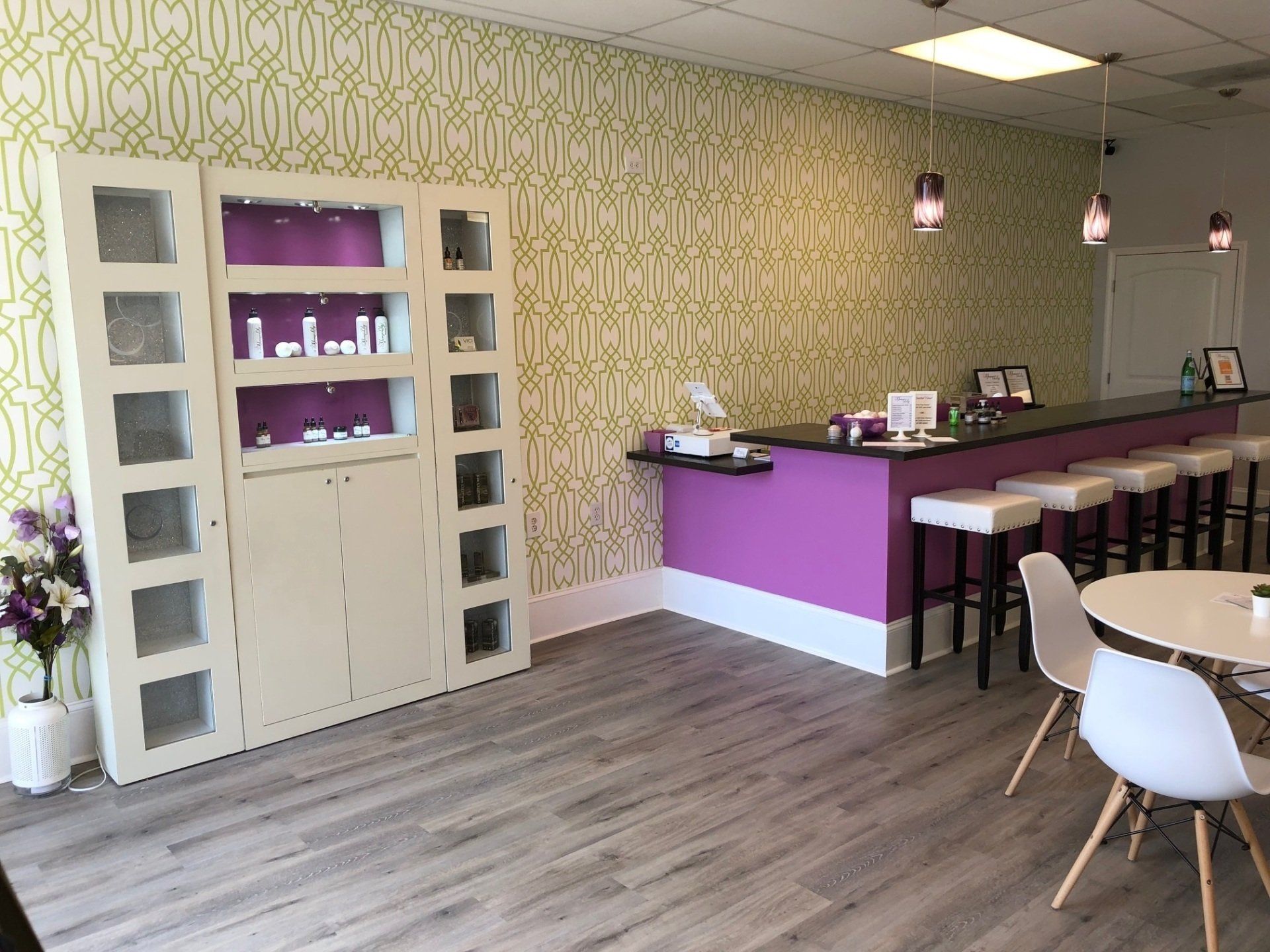 Interior of a retail shop with display case, bar, tables, and patterned wallpaper. Purple and white accents.