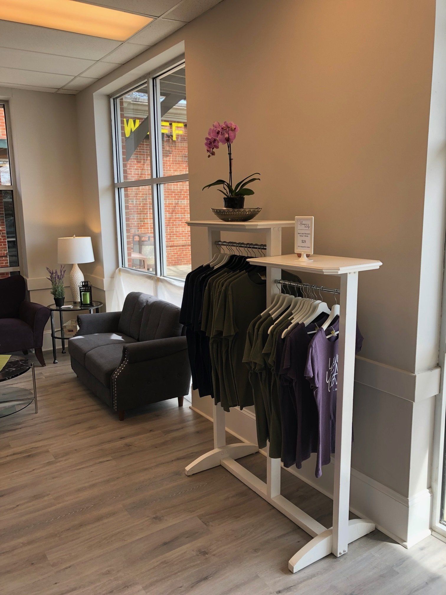 Clothing rack with shirts, near a window and seating in a retail space.