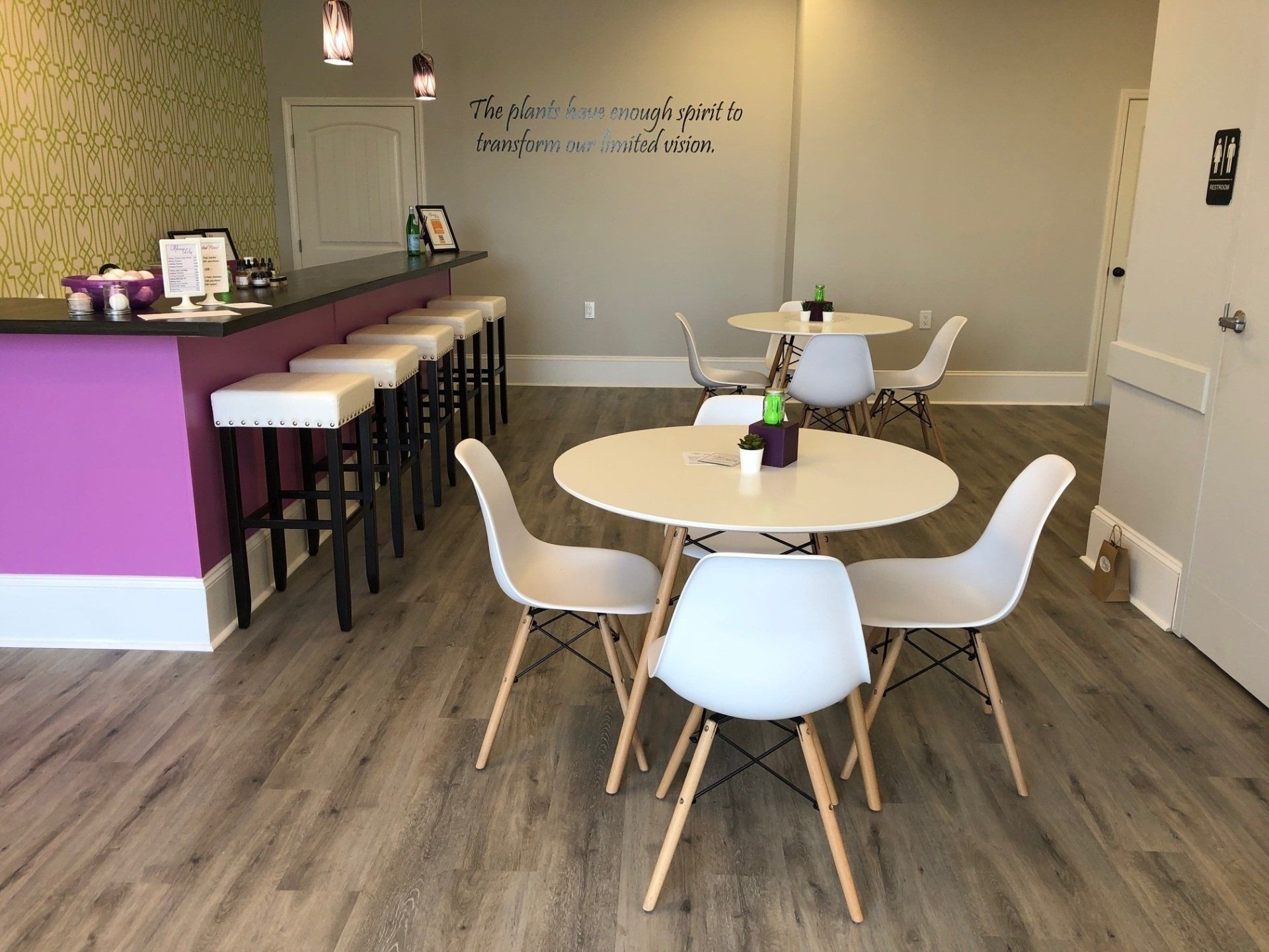 Interior of a cafe with tables, chairs, and a bar with stools. Walls are purple and gray.