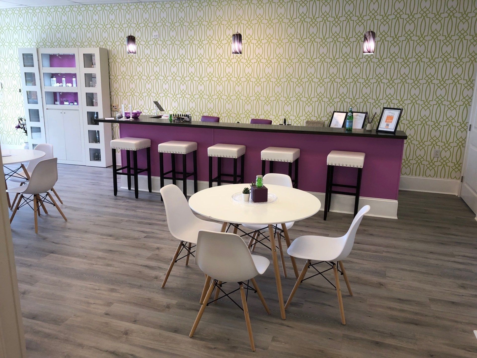 Interior of a nail salon with purple accents, white chairs, and a bar with stools.