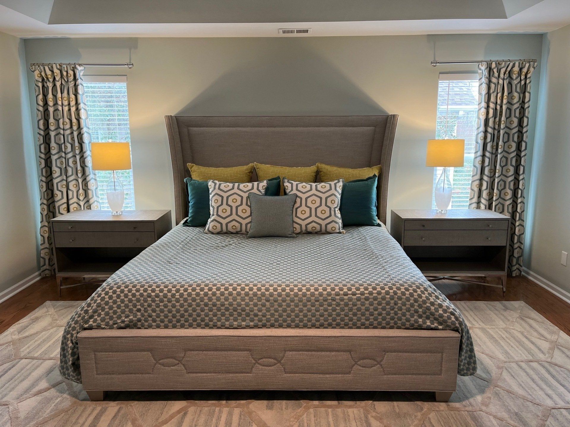 Bedroom with a bed, two nightstands, lamps, and curtains in shades of gray and blue.