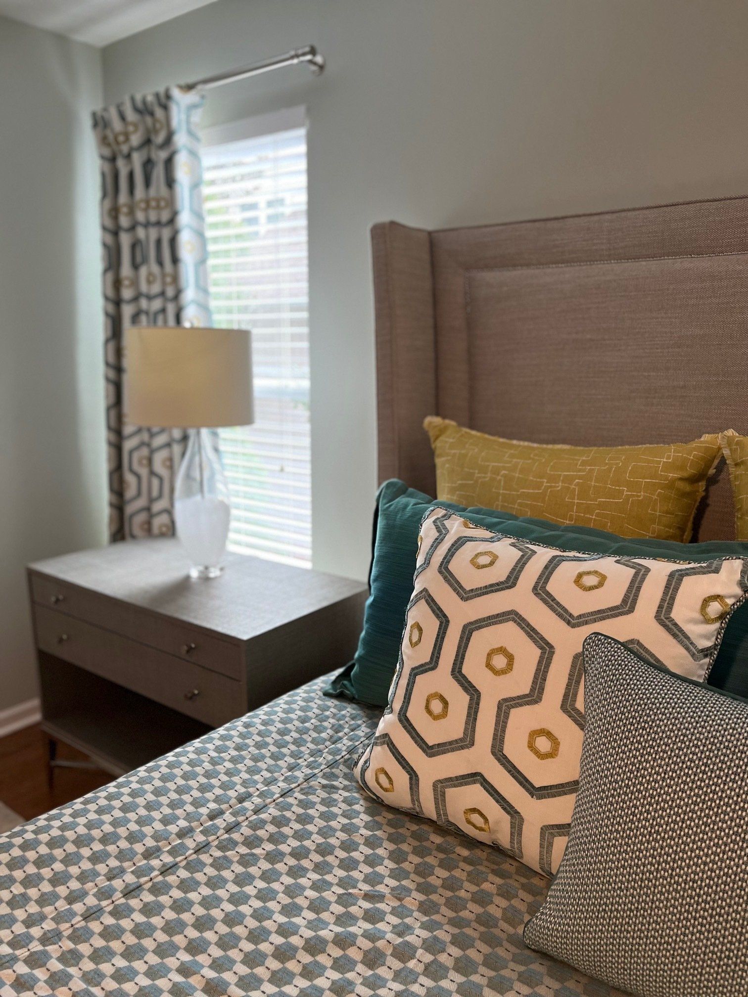 Bedroom with gray upholstered headboard, patterned pillows, and blue and yellow accents.