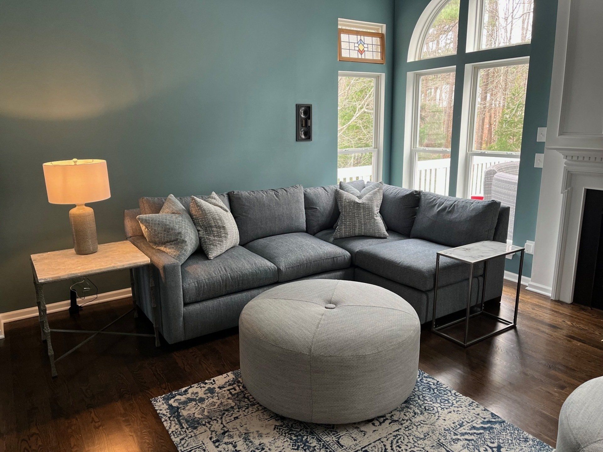 A blue sectional sofa in a living room with a large window and an ottoman.