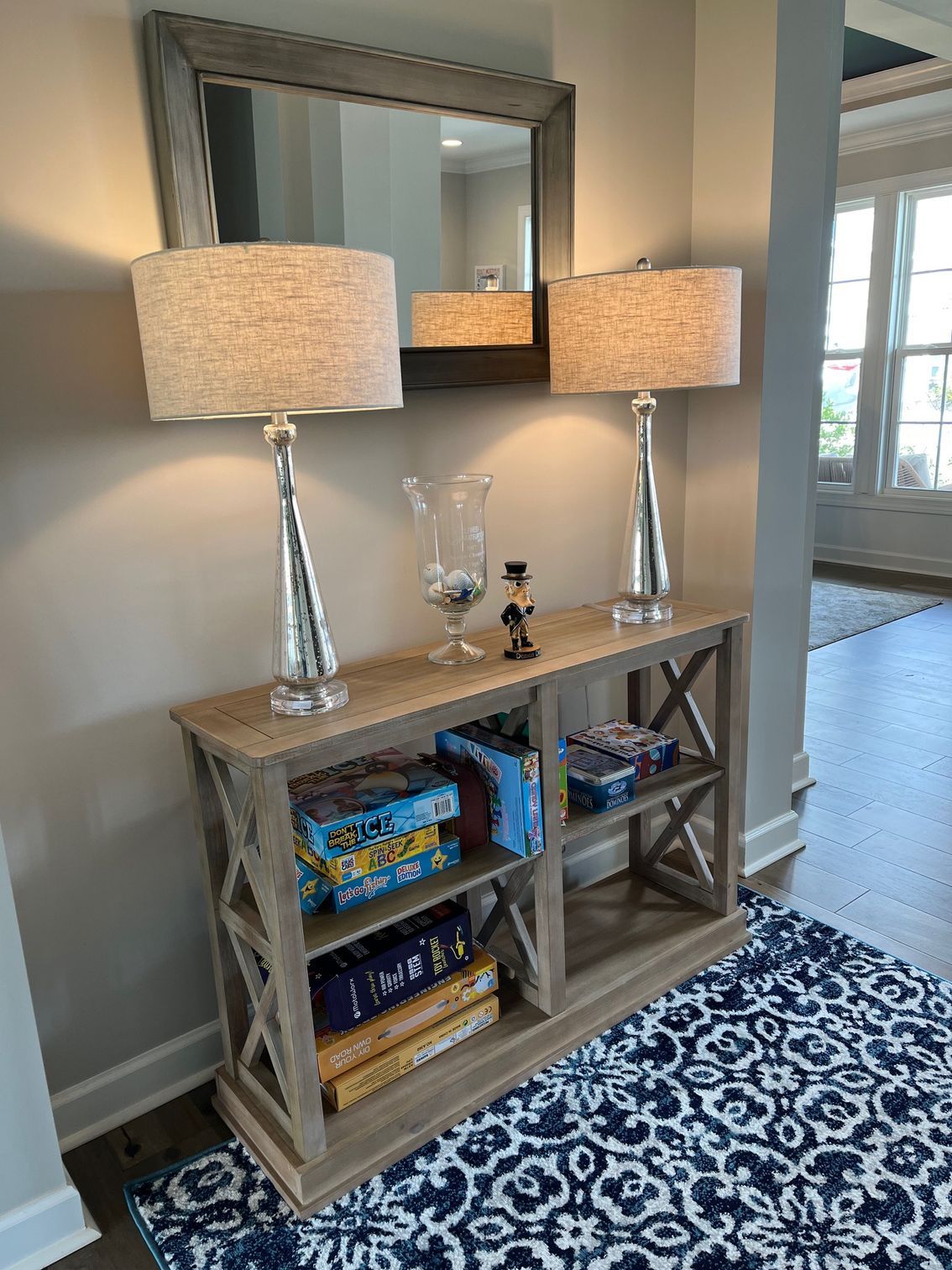 Entryway with console table, lamps, mirror, games, and blue rug.