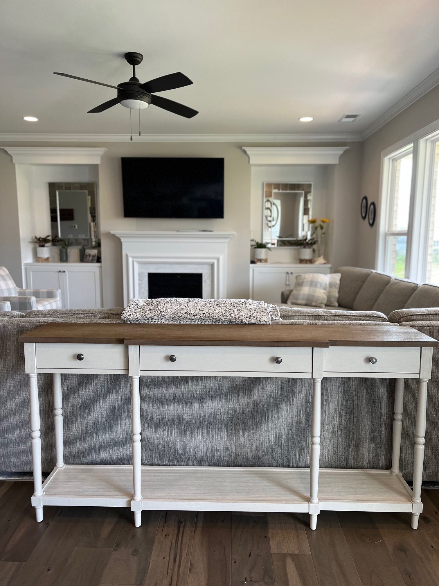 Long, white console table in front of a gray sofa. The setting is a living room with a fireplace and TV.