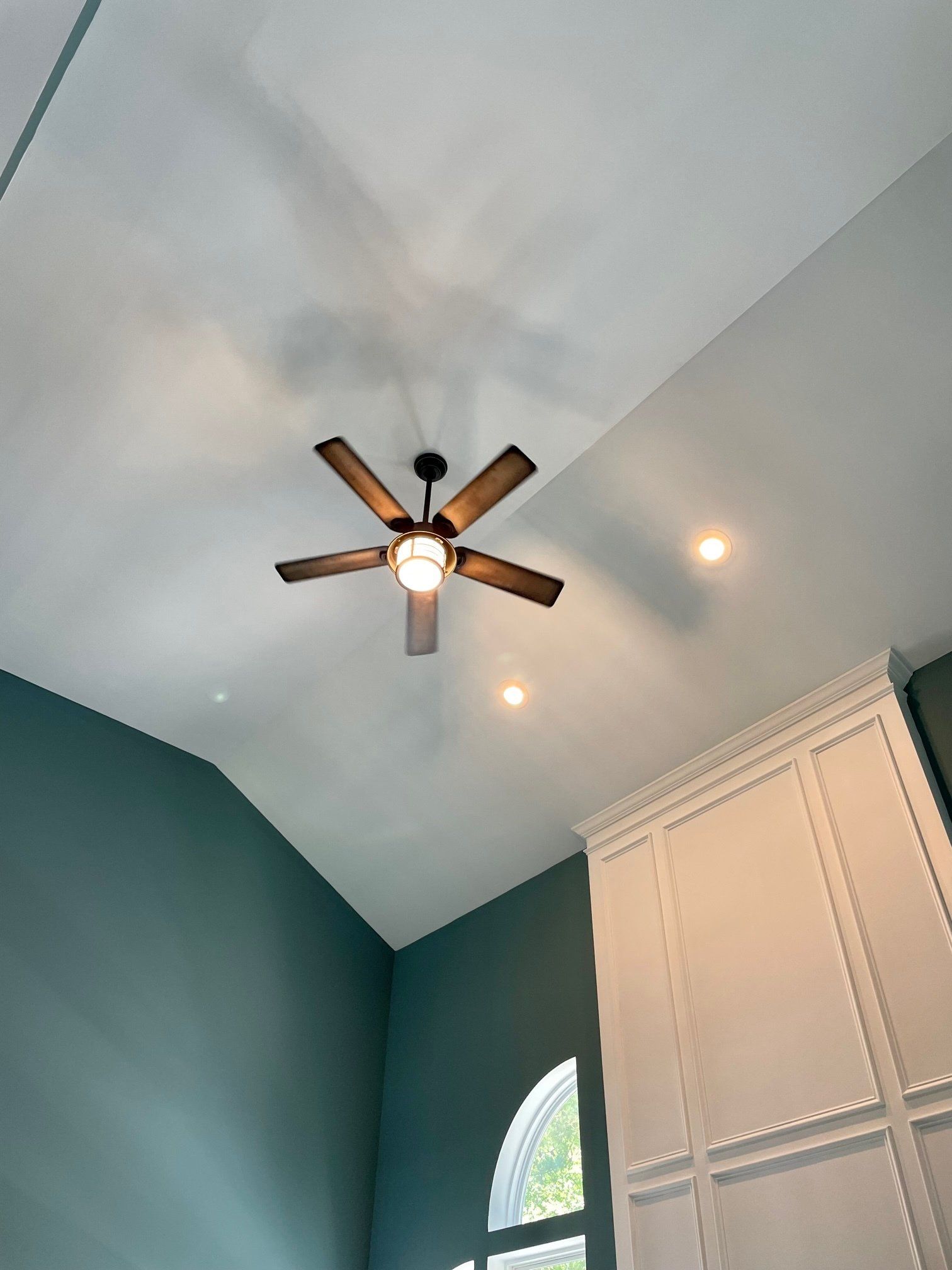 Ceiling fan with light in a room with teal walls and white cabinets.