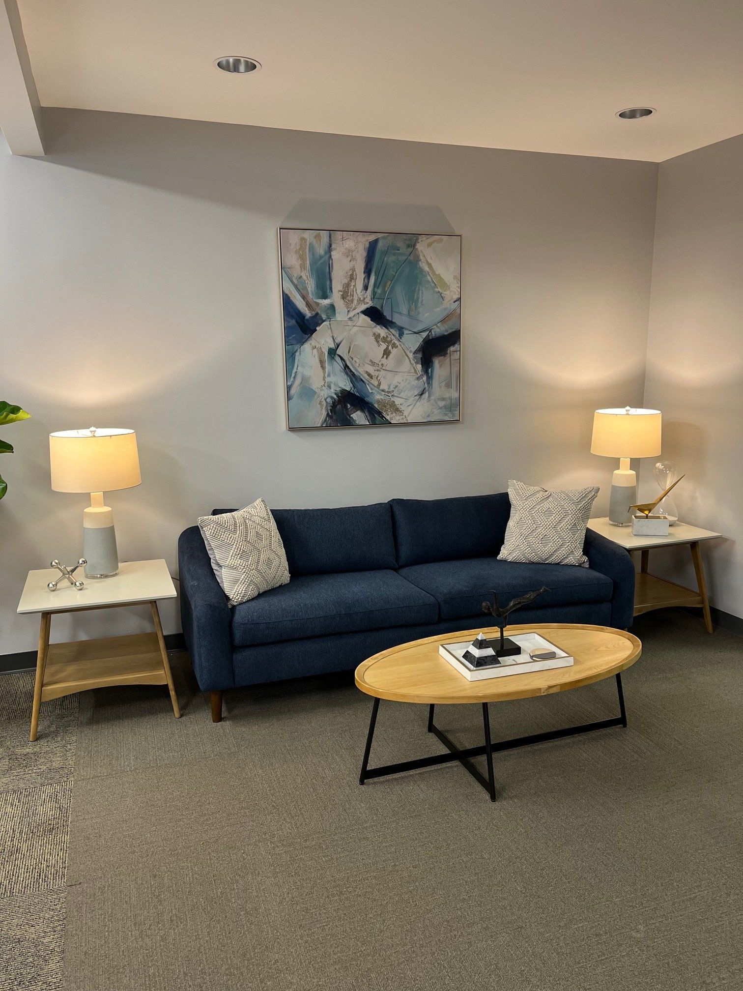 A blue sofa with white accent pillows between two side tables with lamps, art, and a coffee table in a living room.