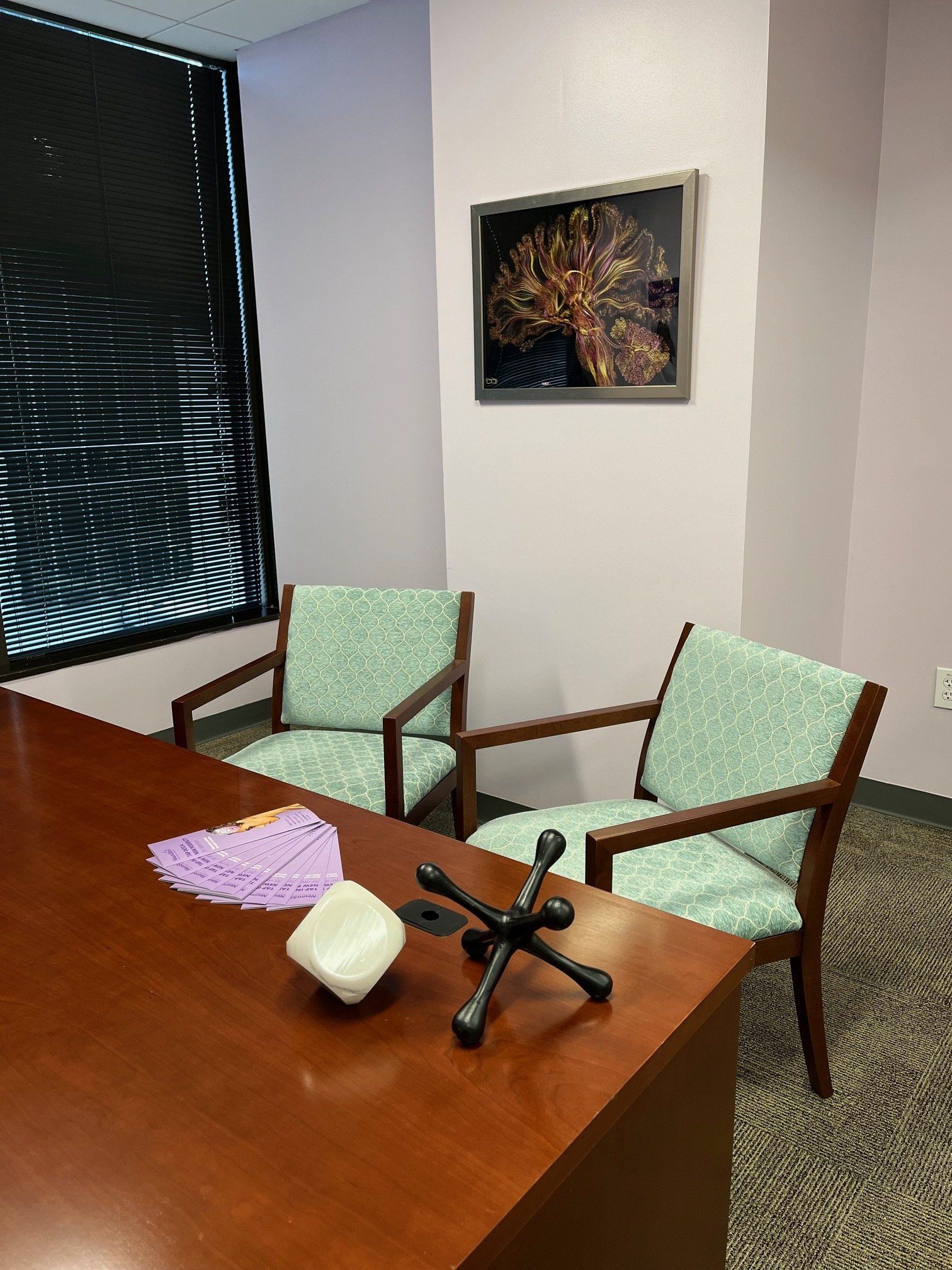 Office with desk, two chairs, and artwork; desk has a decorative jack, small white sculpture, and papers.