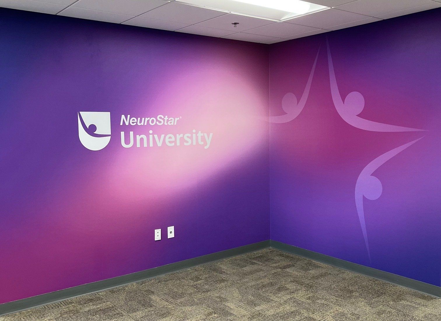 Purple wall with NeuroStar University logo and abstract figures in an office setting.