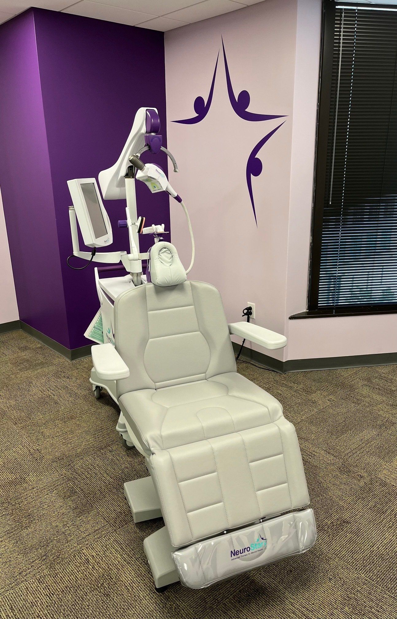 Medical examination chair in a room with purple accents and yoga-themed wall art.