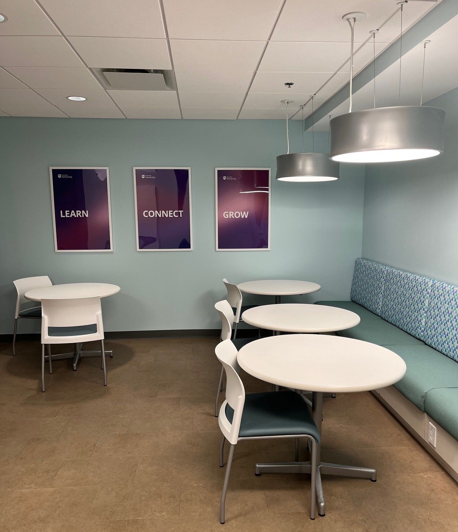 A room with round white tables, chairs, and a built-in blue bench, plus three framed posters.