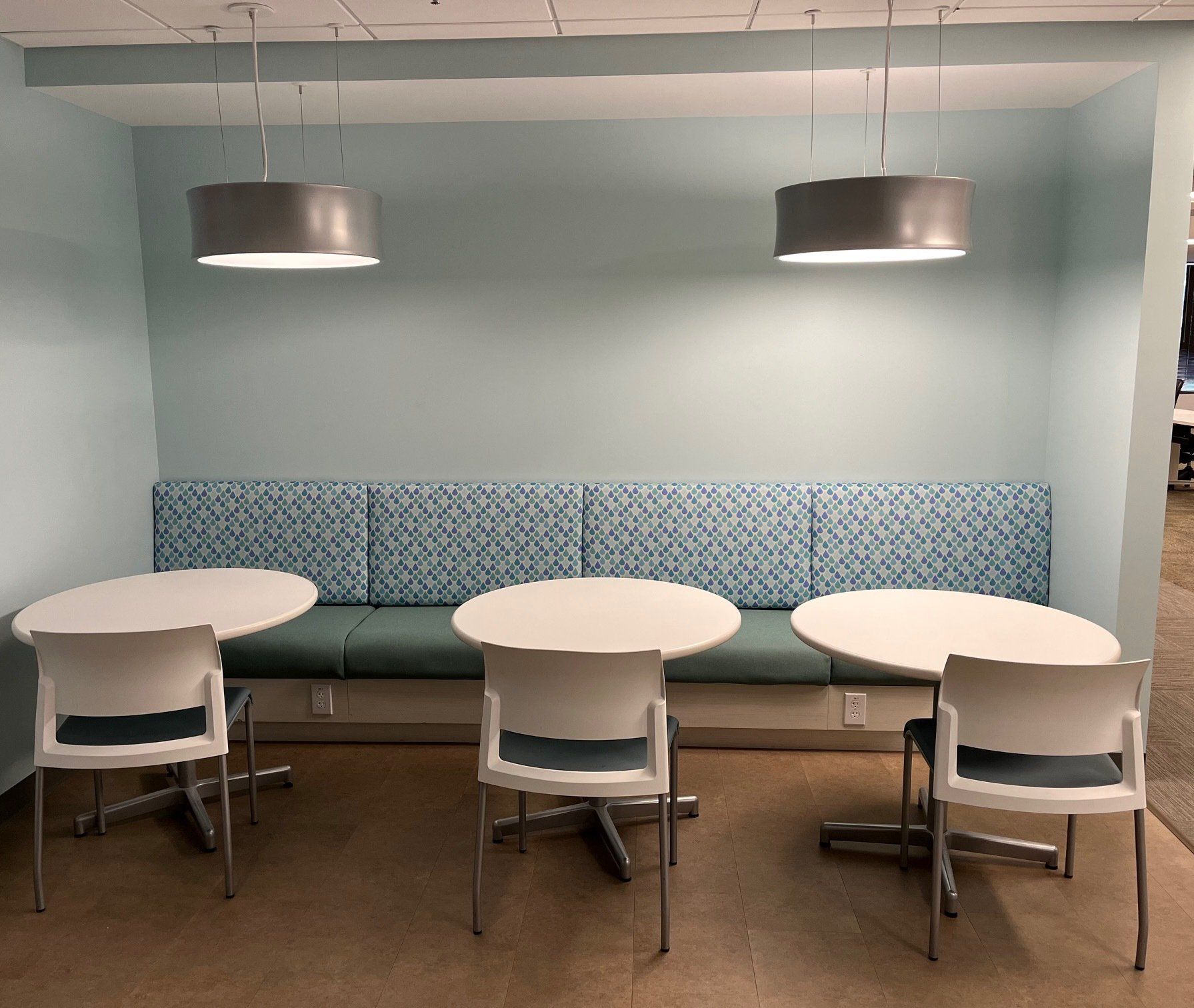 A seating area with three white tables, chairs, and a built-in blue cushioned bench with hanging lamps above.
