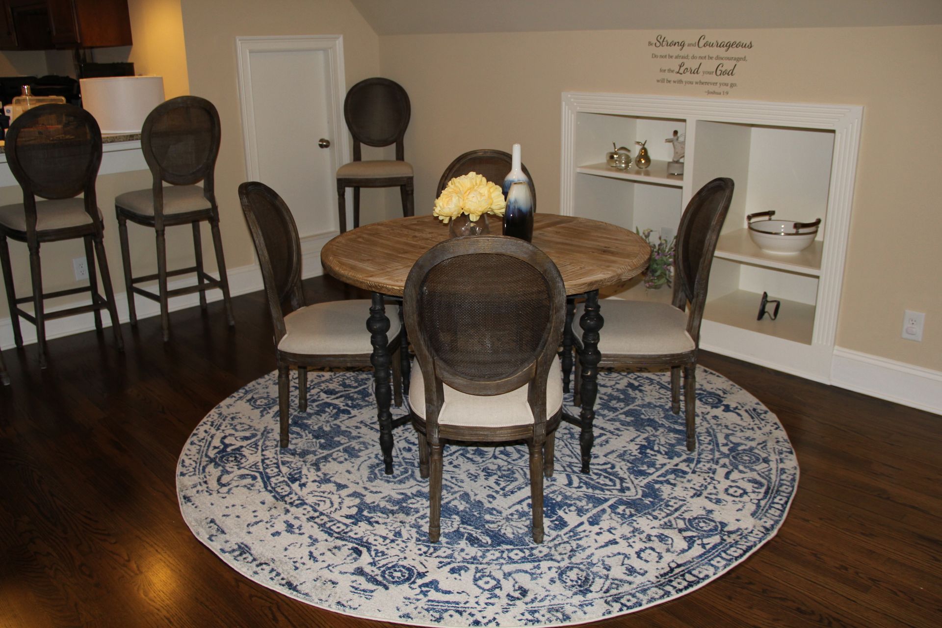A dining area with a round table, six chairs, and a blue patterned rug.