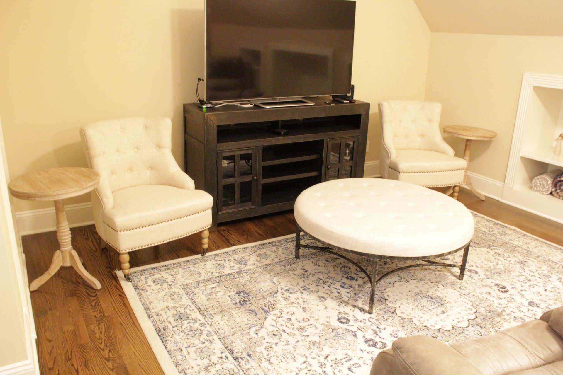 Living room with TV, two chairs, an ottoman, rug, and side tables.