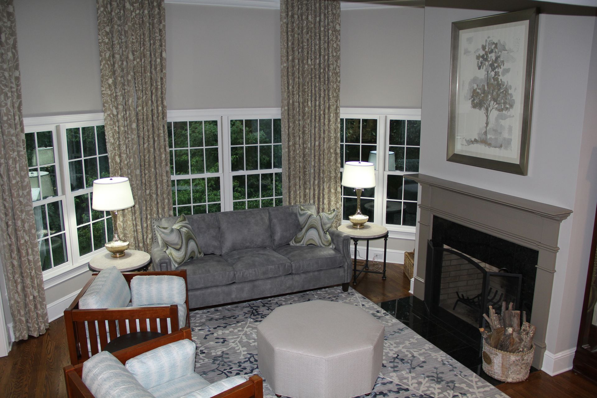 Living room with gray walls, fireplace, windows, gray sofa, and patterned curtains.