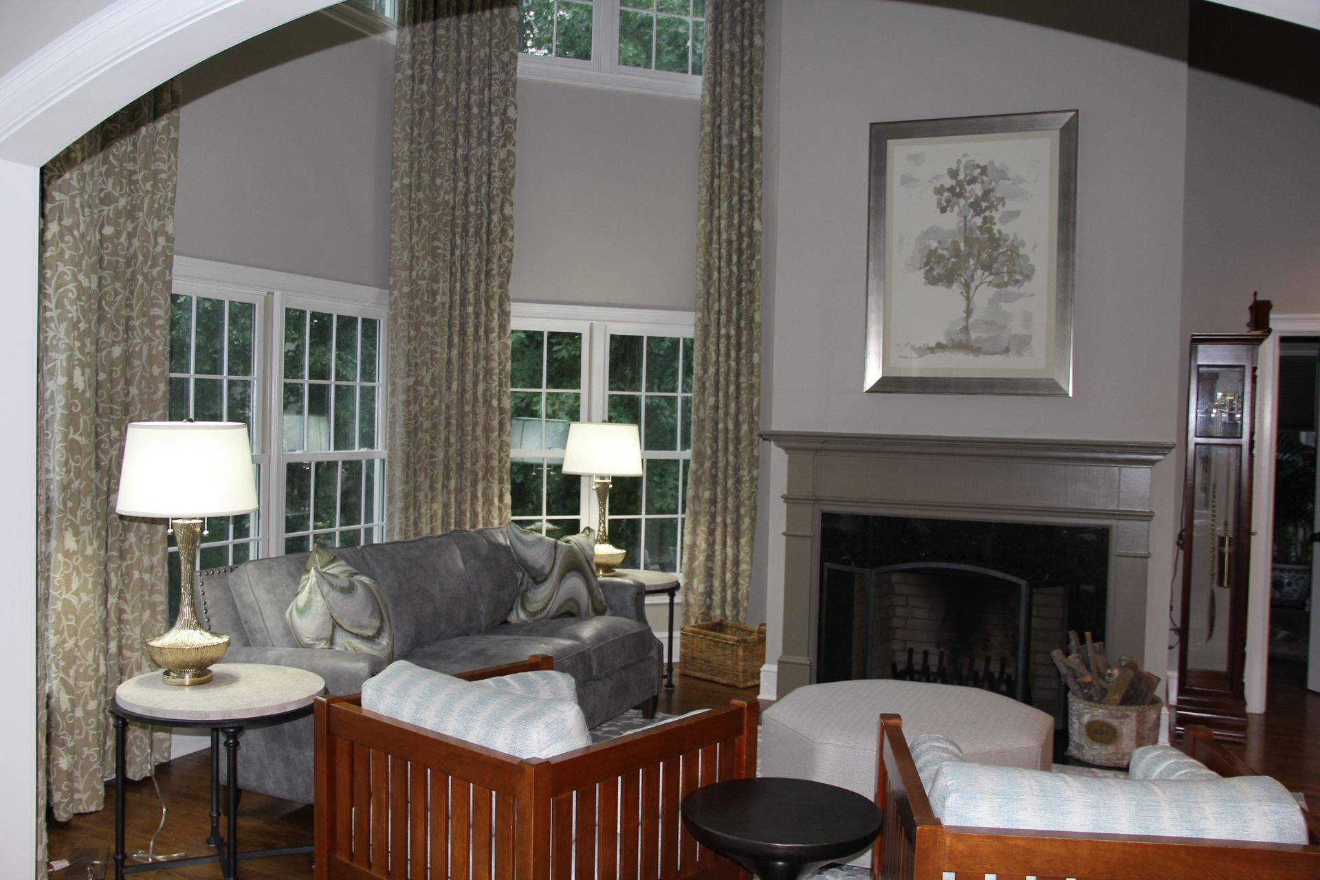 Living room with high ceiling, fireplace, sofa, armchairs, and patterned curtains.