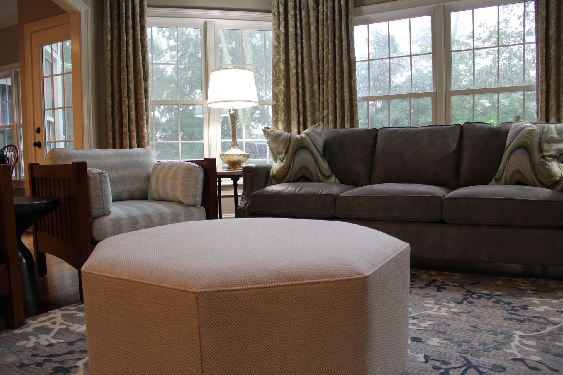 Living room with gray sofa, patterned curtains, ottoman, armchair, and table lamp.