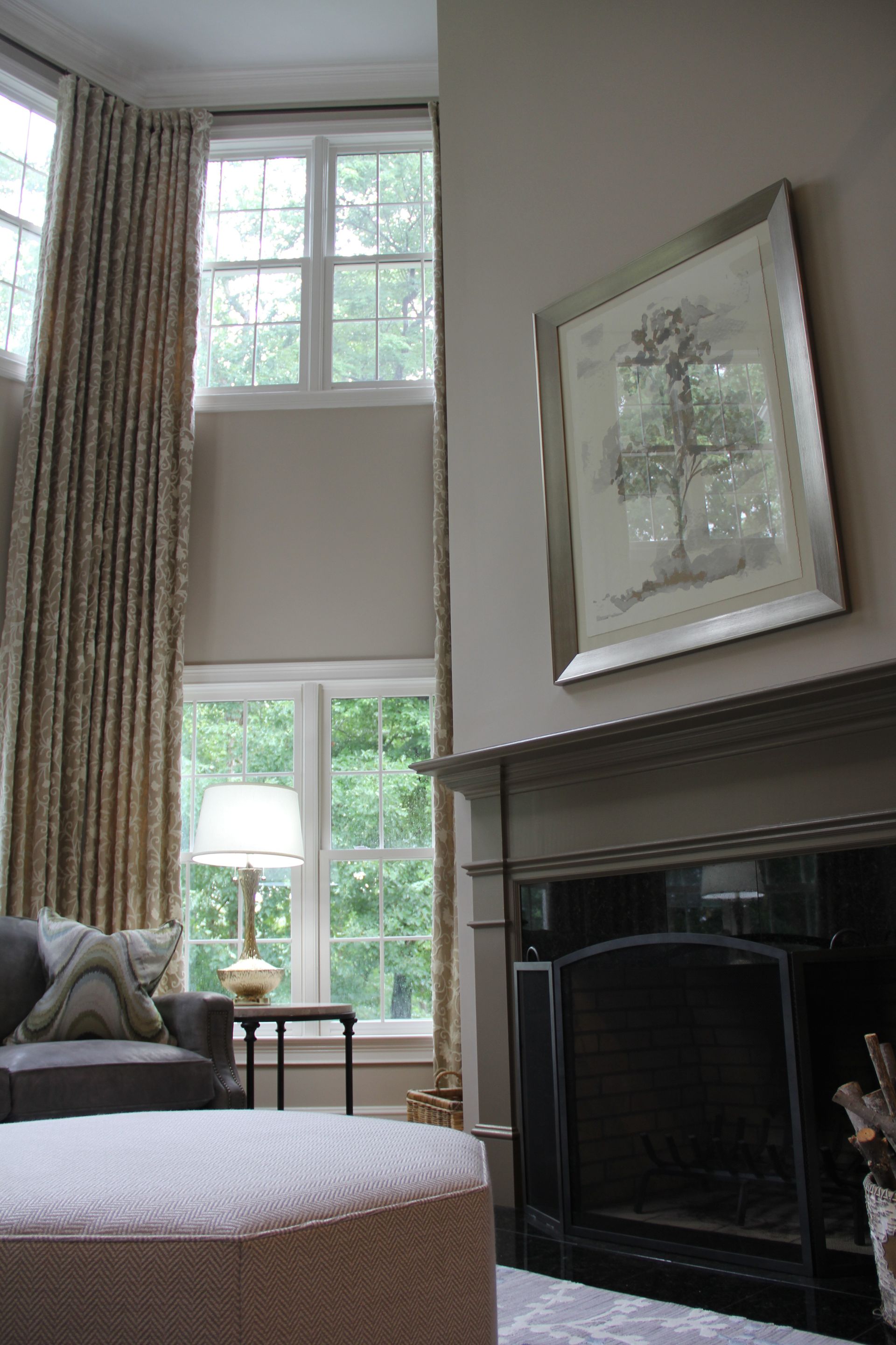 Living room with tall windows, neutral walls, fireplace, and a decorative ottoman.