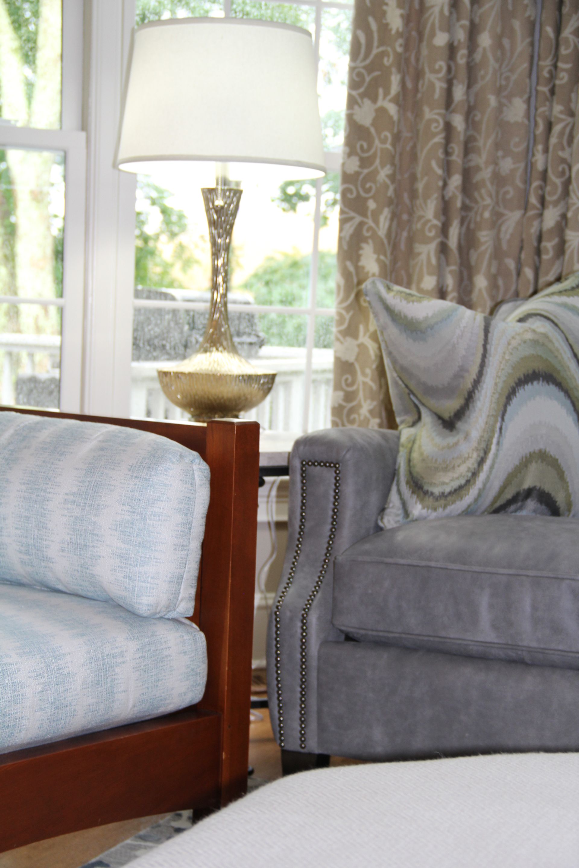 Two armchairs in a living room with a lamp and a window, various patterned pillows and curtains.