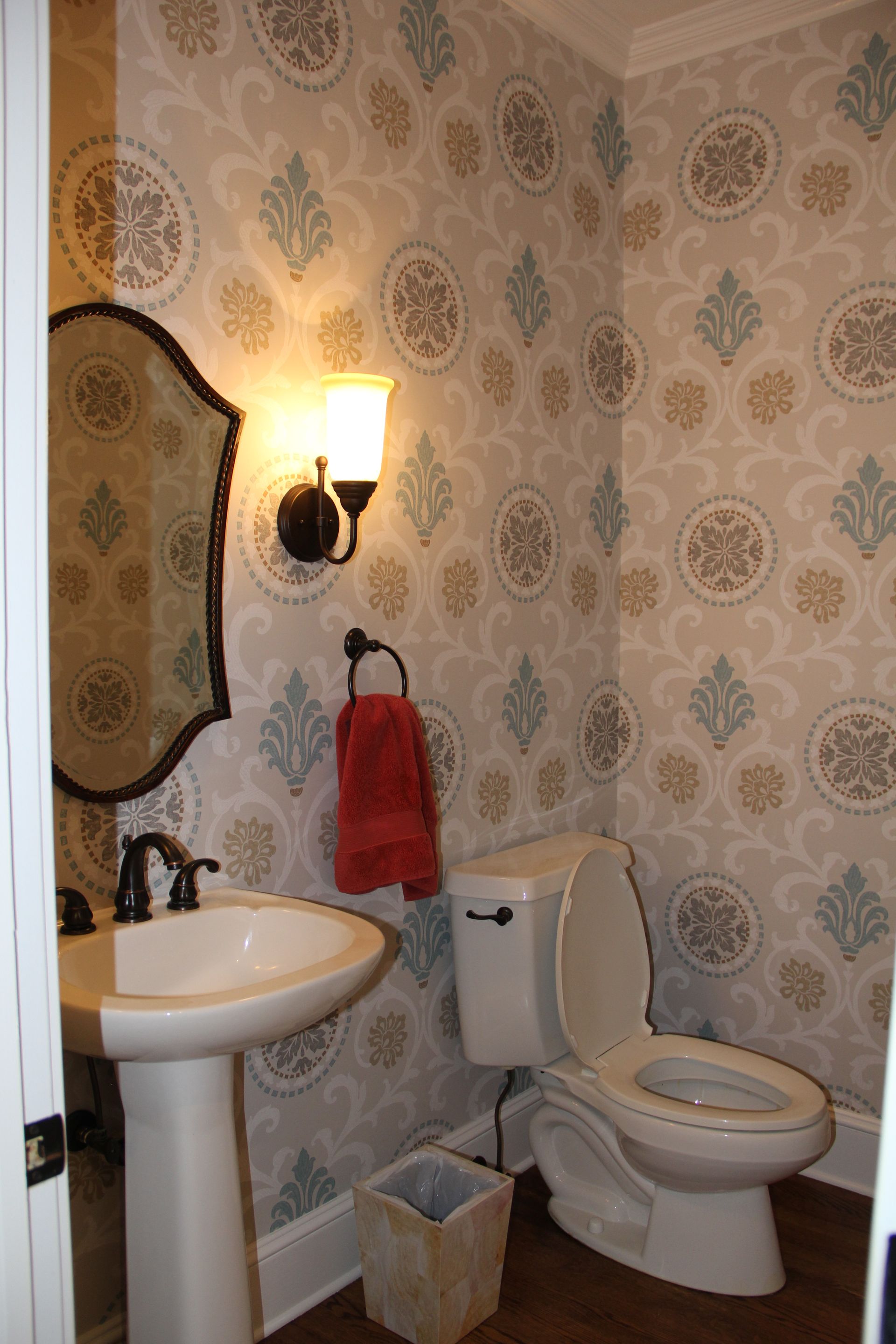 Small bathroom with patterned wallpaper, sink, toilet, and red towel.