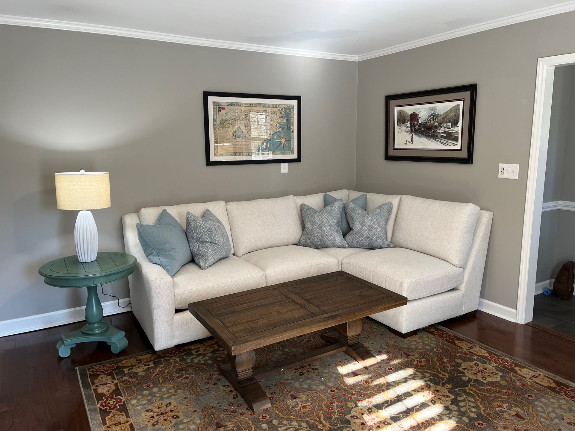 A corner sofa in a gray-walled room. Light blue pillows, wooden coffee table, green side table, and art.